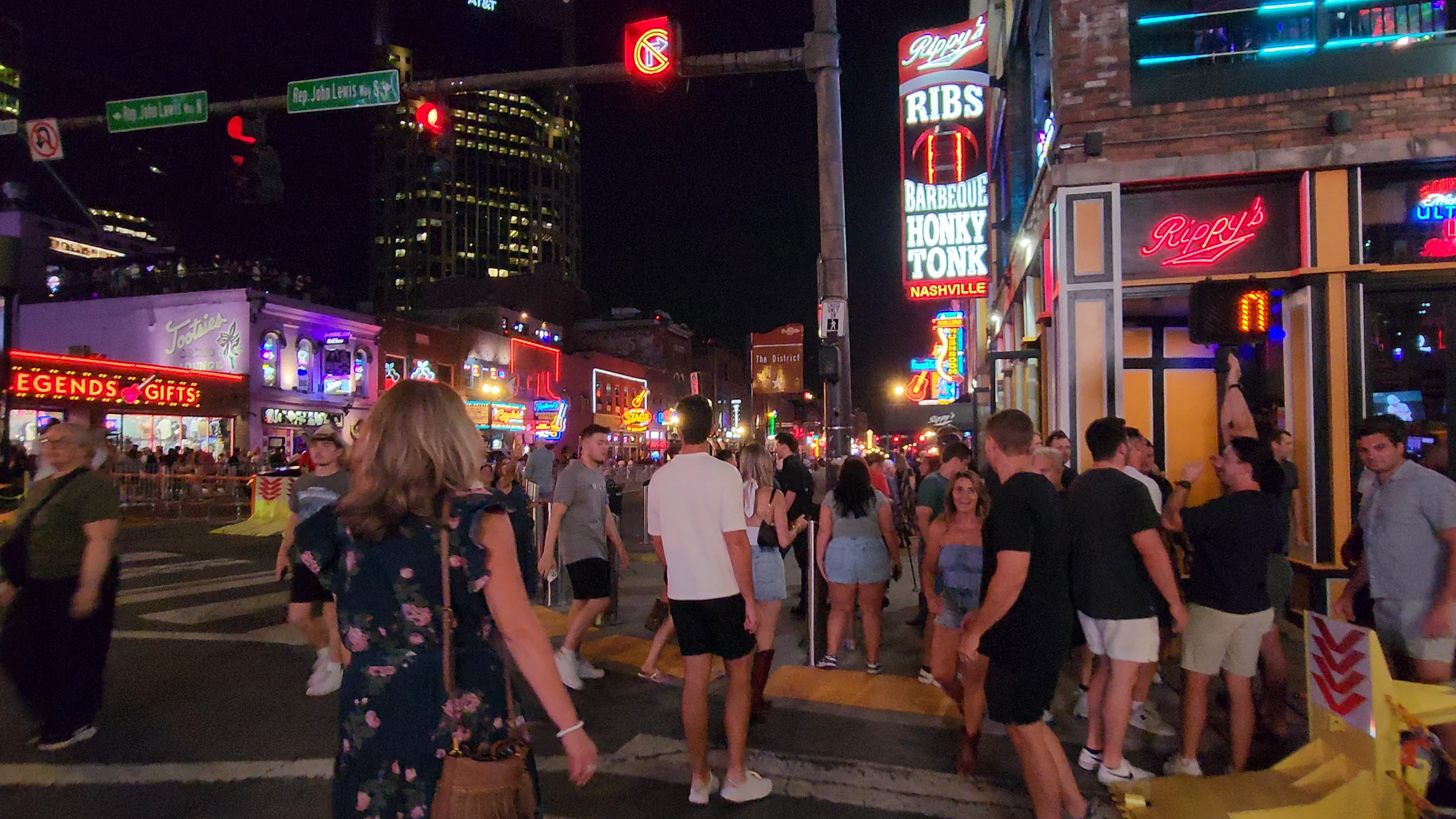 People walk past Rippy's illuminated signs at the Broadway and Fifth Avenue intersection at night.